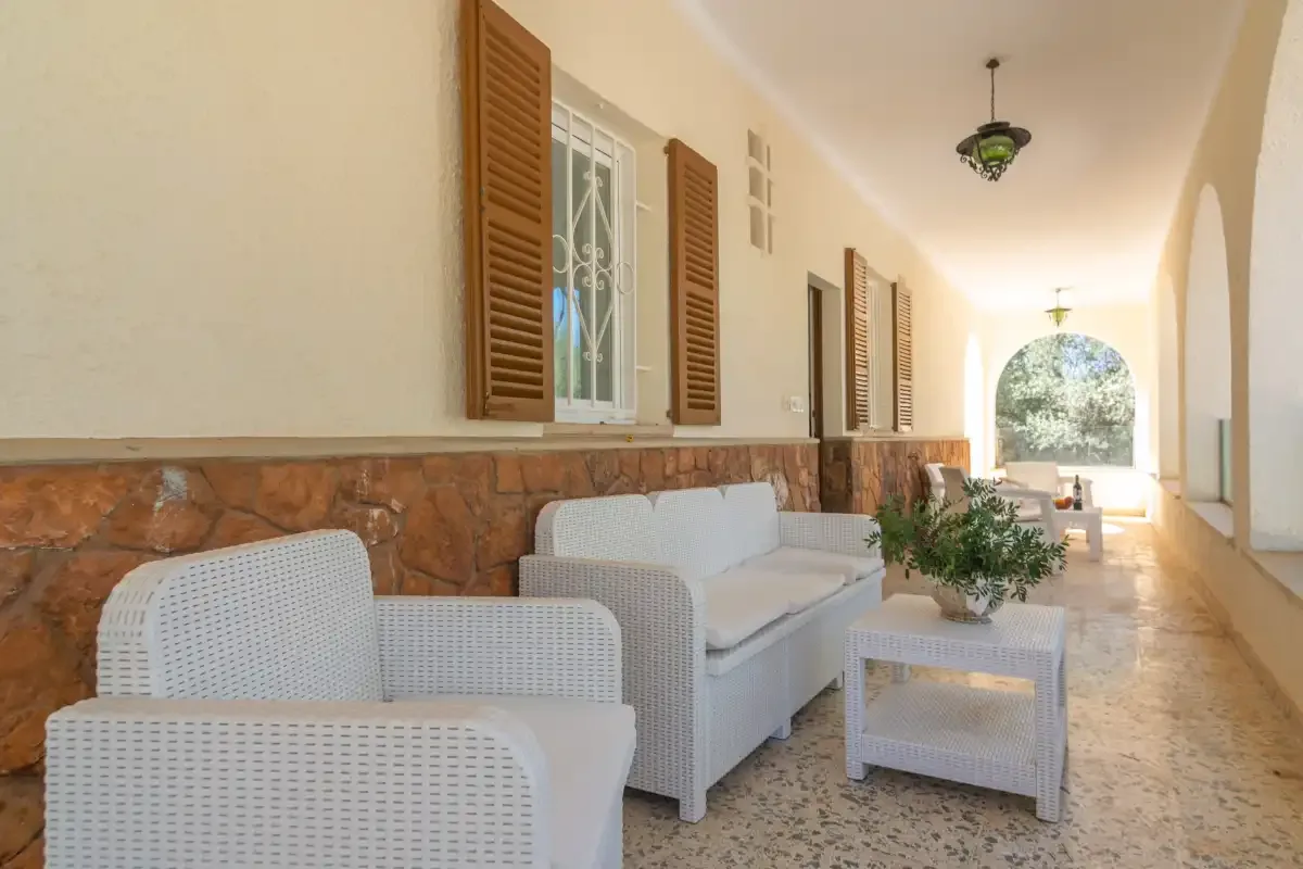 A covered outdoor seating area with white wicker furniture and a low table.