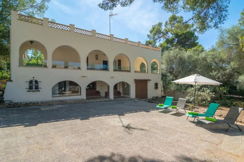 A pale two-story building with arched openings overlooks a paved outdoor area.