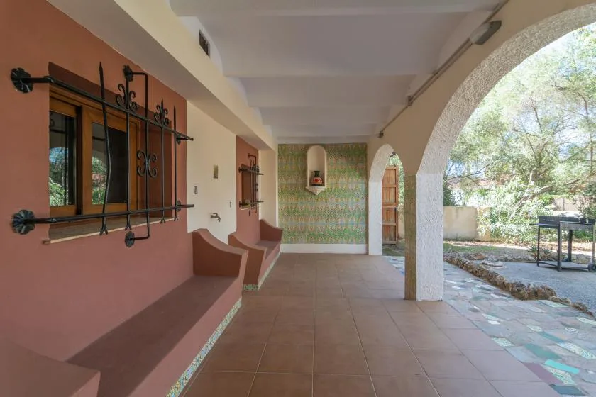 A covered patio with arched openings, tiled flooring, and a window with metal bars.