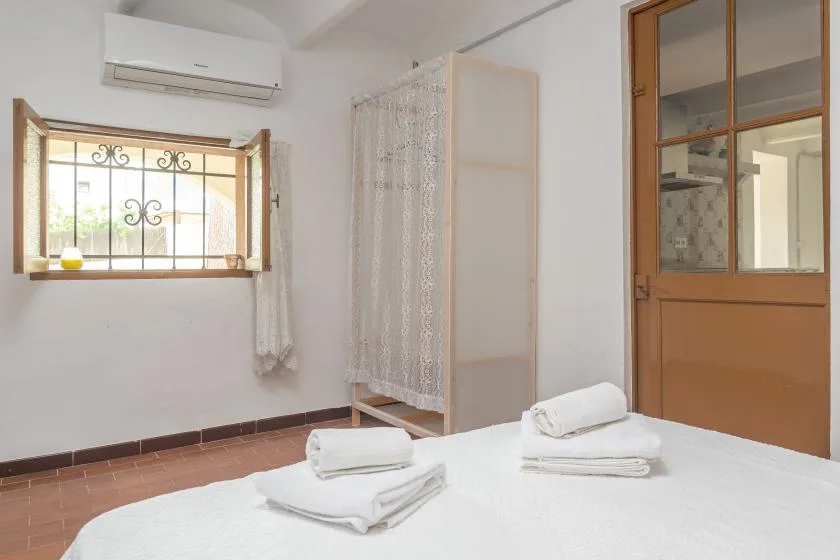 A bright bedroom with a bed, folded towels, and a curtained shower area.