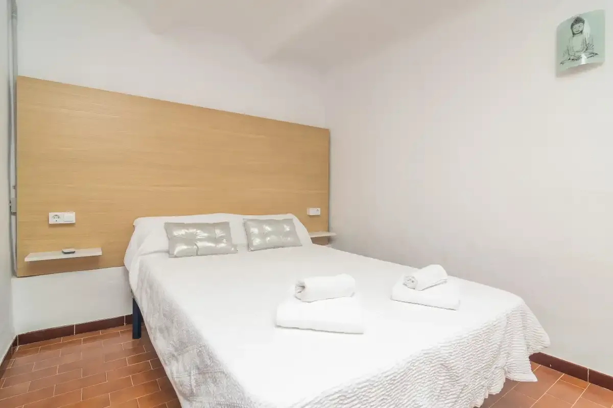 A bedroom with a double bed, white bedding, and a wooden headboard.