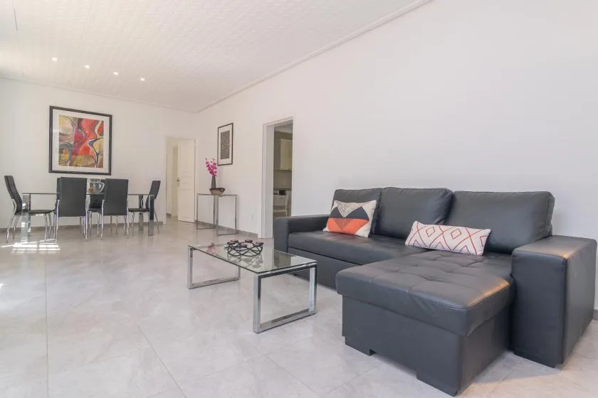 A bright living and dining area with dark seating and a glass coffee table.
