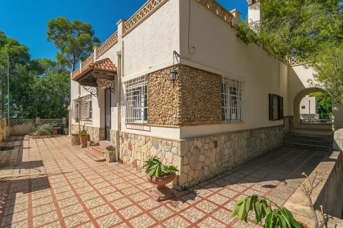 A house exterior with a tiled patio and plants beside the walkway.