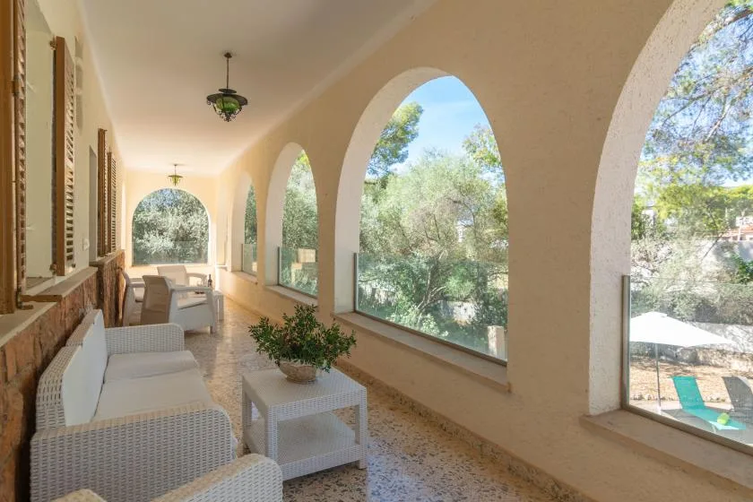 A covered veranda with seating overlooks trees through large arched openings.