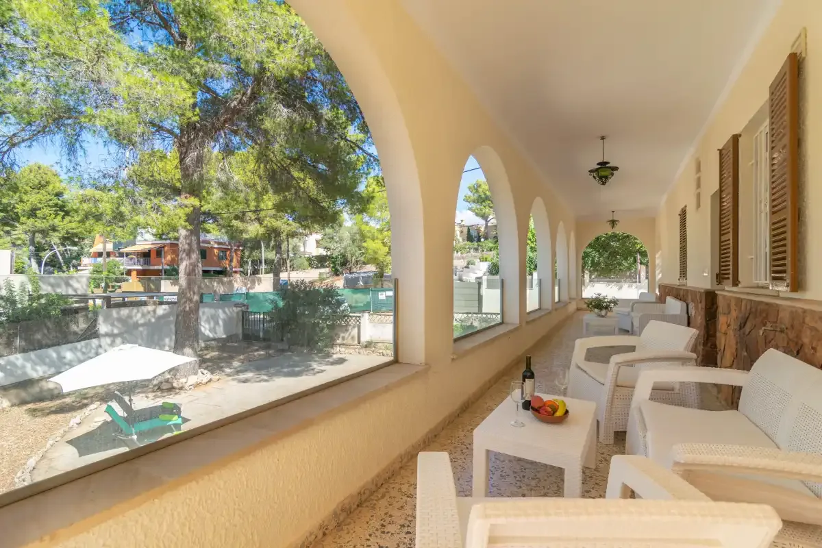 A covered patio with seating overlooks a garden through a row of arches.