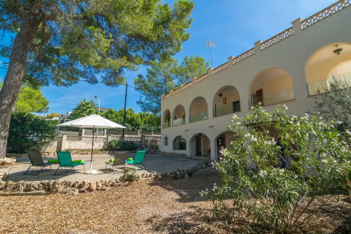 A villa exterior with arched balconies beside a tree-shaded patio.