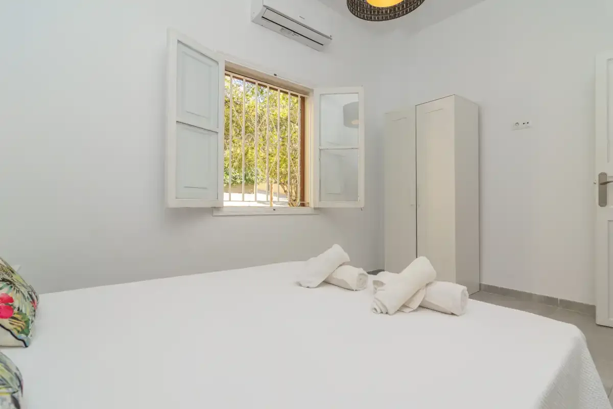 A bright bedroom with a white bed beneath an open window.