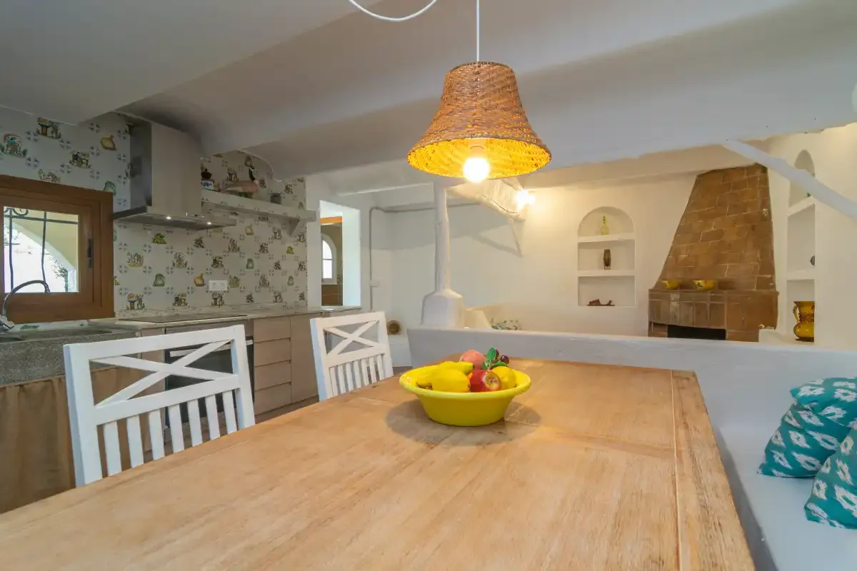 A dining area with a wooden table beside a kitchen and brick fireplace.