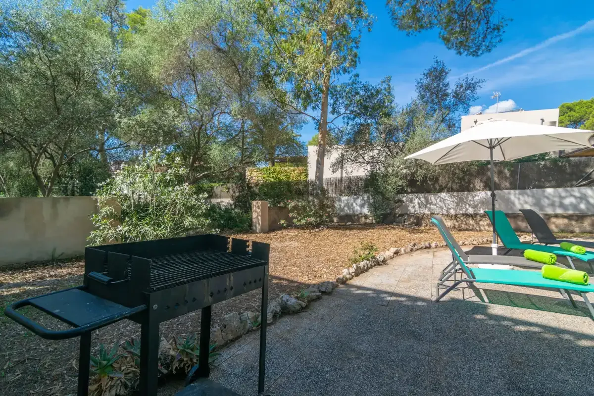 An outdoor patio with a barbecue and lounge chairs beneath a large umbrella.