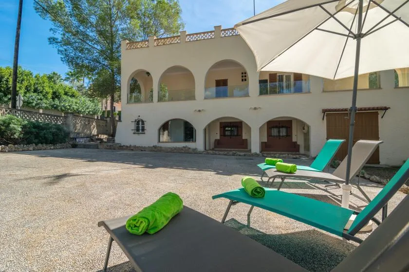 A sunny courtyard with lounge seating, green towels, and a large umbrella.
