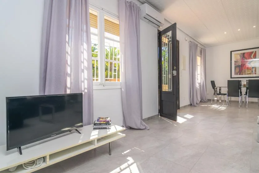 A bright living area with a television, tall windows, and a dining table.