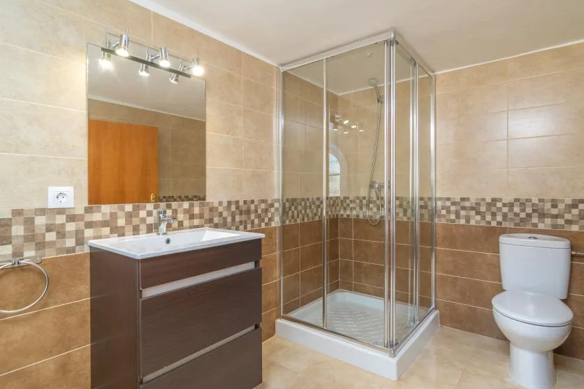 A tiled bathroom with a vanity, glass shower, and toilet.