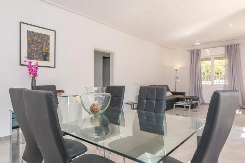 A bright dining and living area with a glass table and seating.