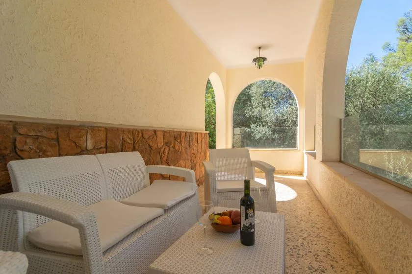 A covered patio with cushioned seating and arched openings overlooking greenery.