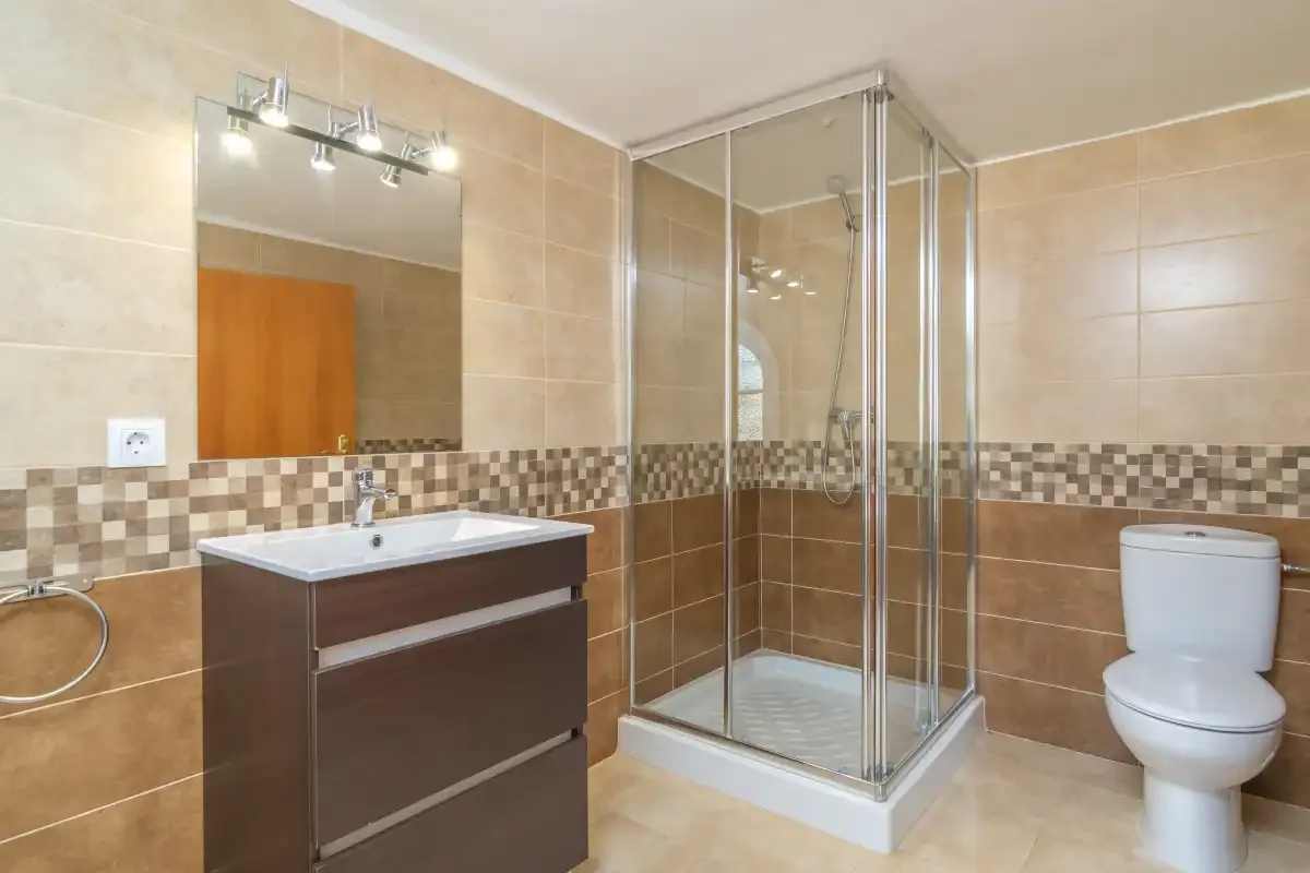 A tiled bathroom with a vanity, glass shower, and toilet.