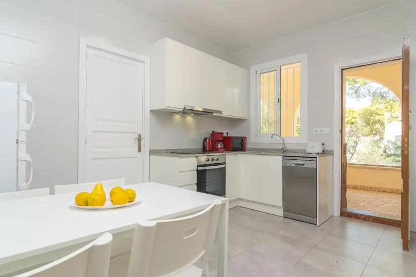 A bright kitchen with white cabinets, a dining table, and an open doorway.