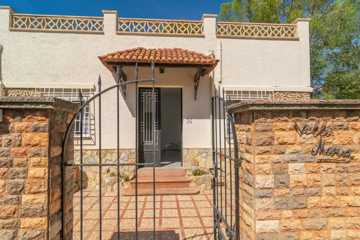 A stucco building entrance has tiled steps, a small tiled canopy, and an iron gate.