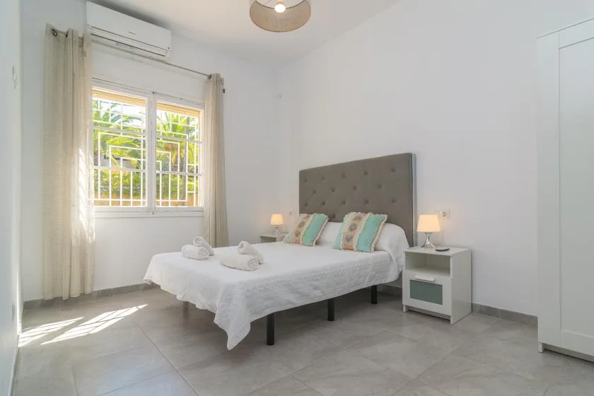 A bright bedroom with a bed beside a sunlit window.