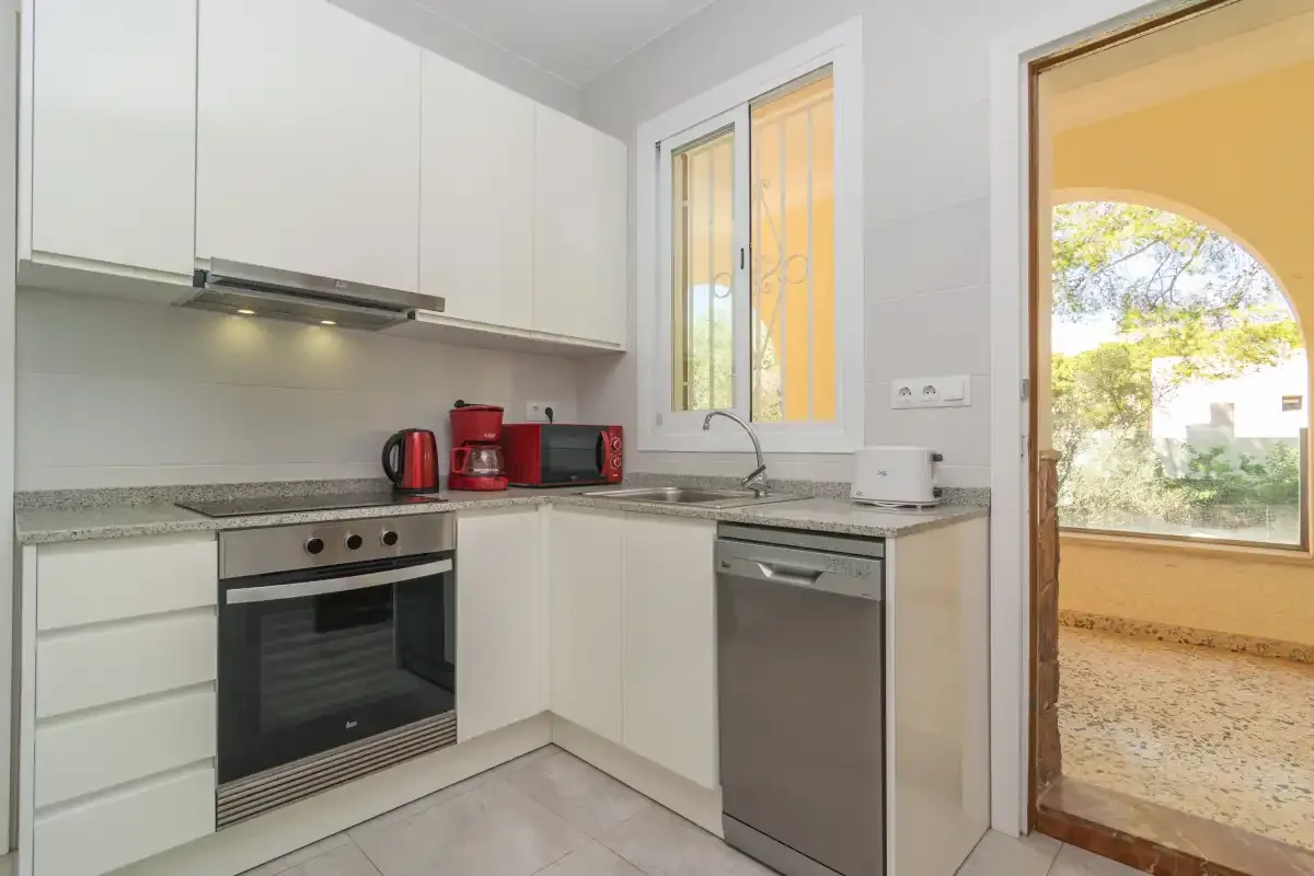 A bright white kitchen with built-in appliances and a window overlooking an outdoor area.