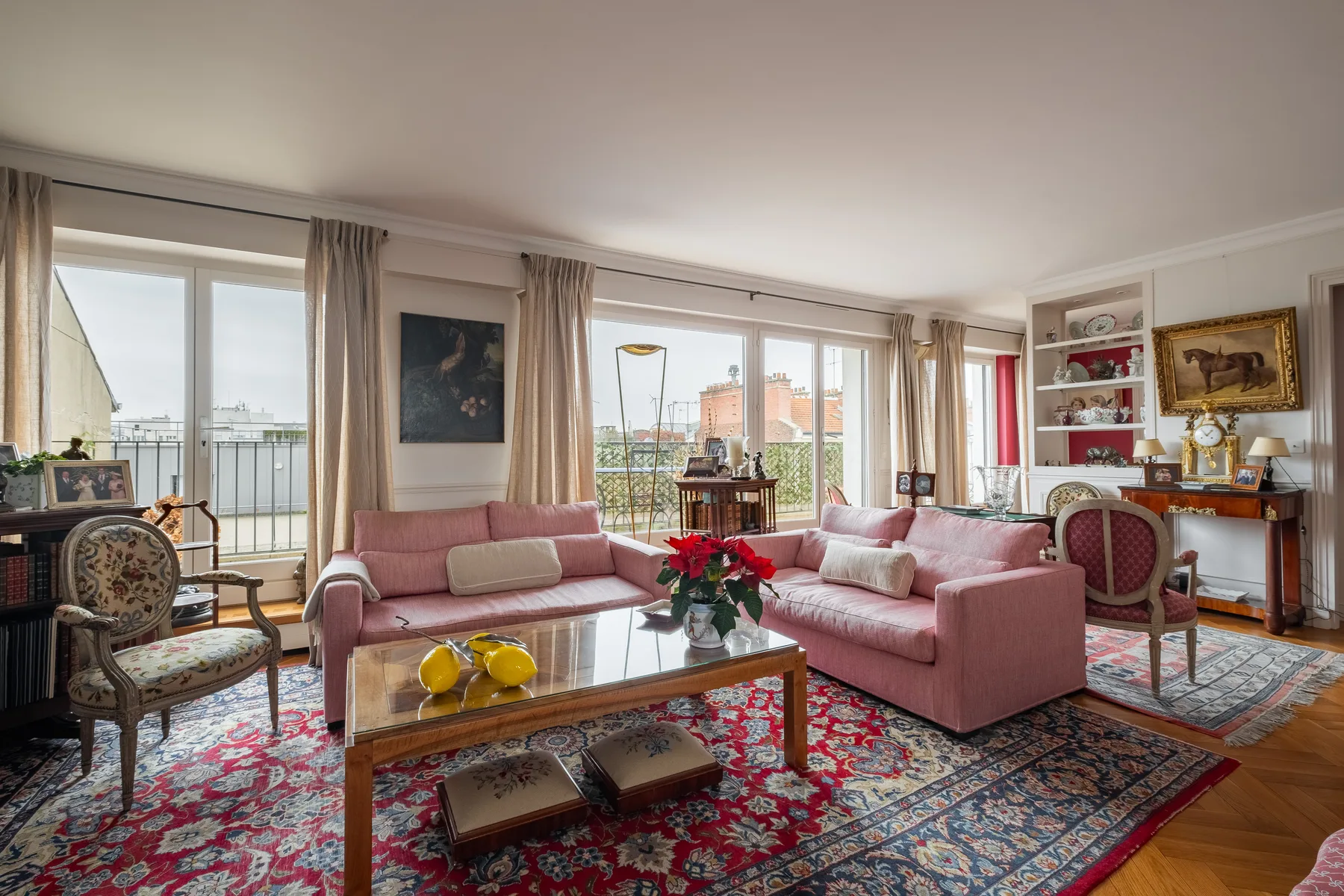 A bright living room with pink seating, a glass coffee table, and large windows.
