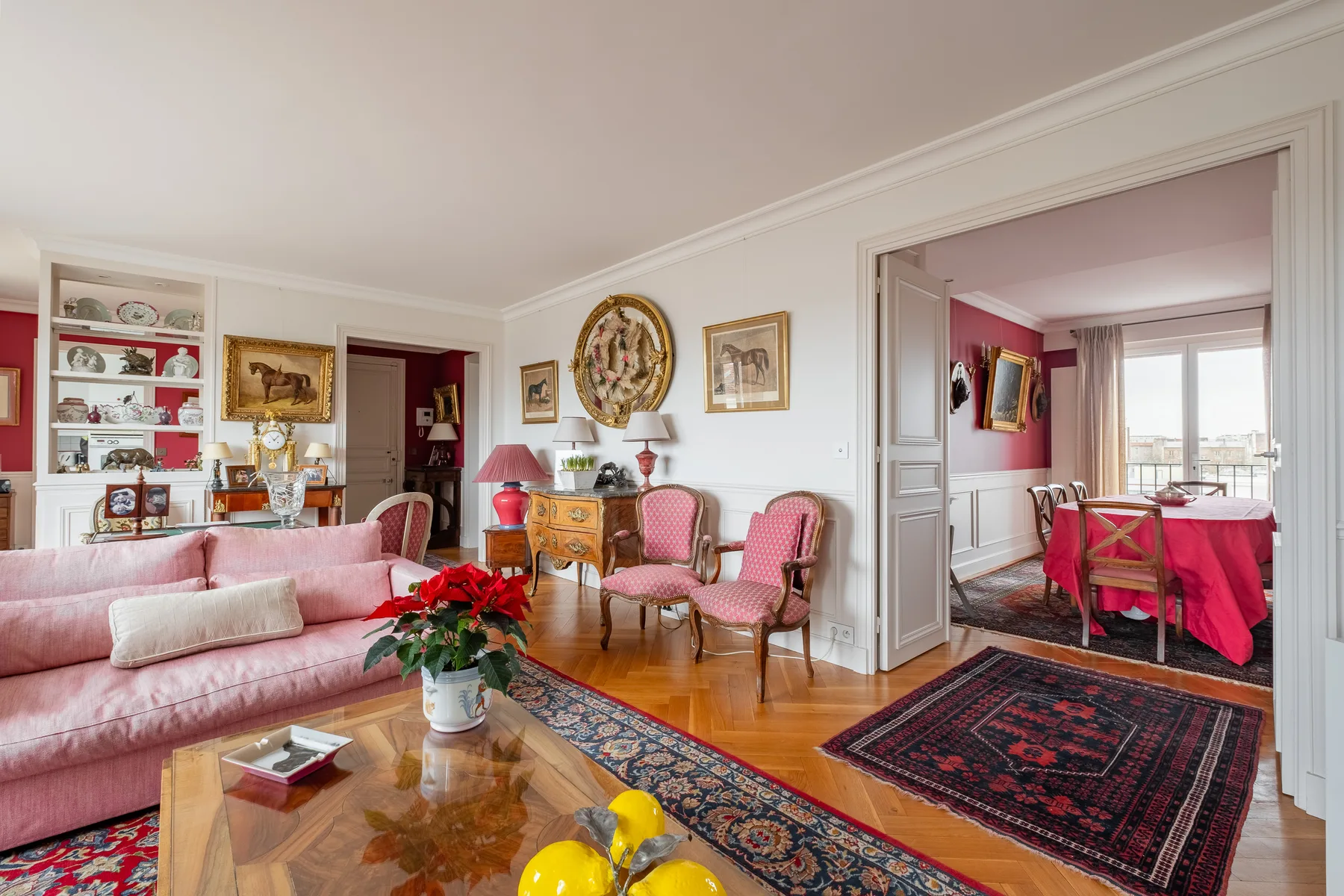 A sitting room with pink seating, a coffee table, and an open doorway to a dining area.