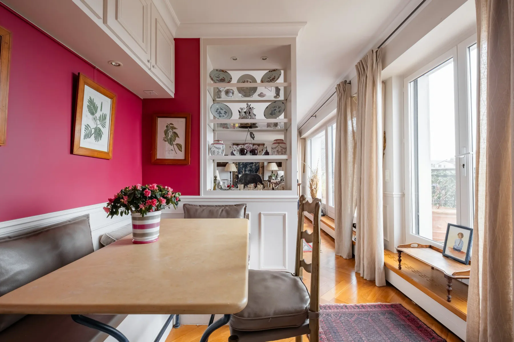 A dining area with a table beside a bright wall of windows.