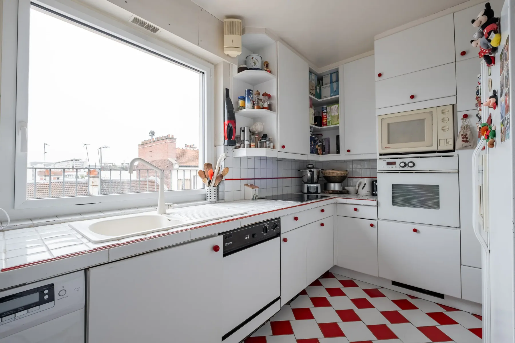 A bright kitchen with white cabinets and a red-and-white checkerboard floor.