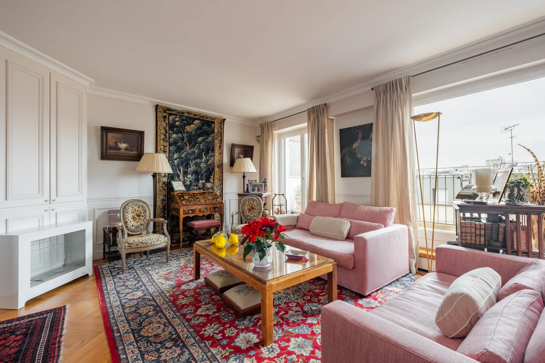 A living room with pink seating, patterned rugs, and doors opening onto a balcony.