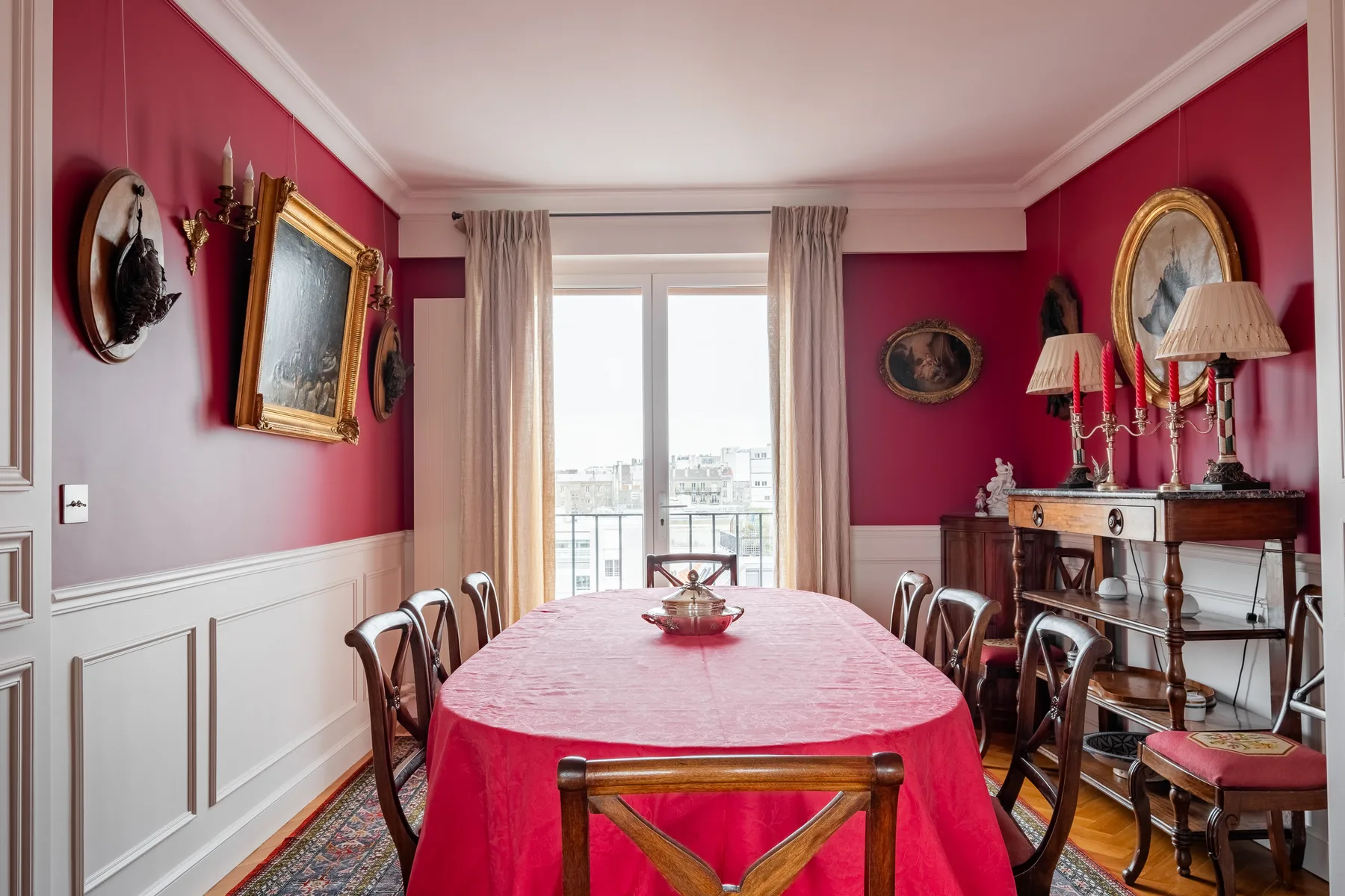 A dining room with a red-covered table set beside a bright window.