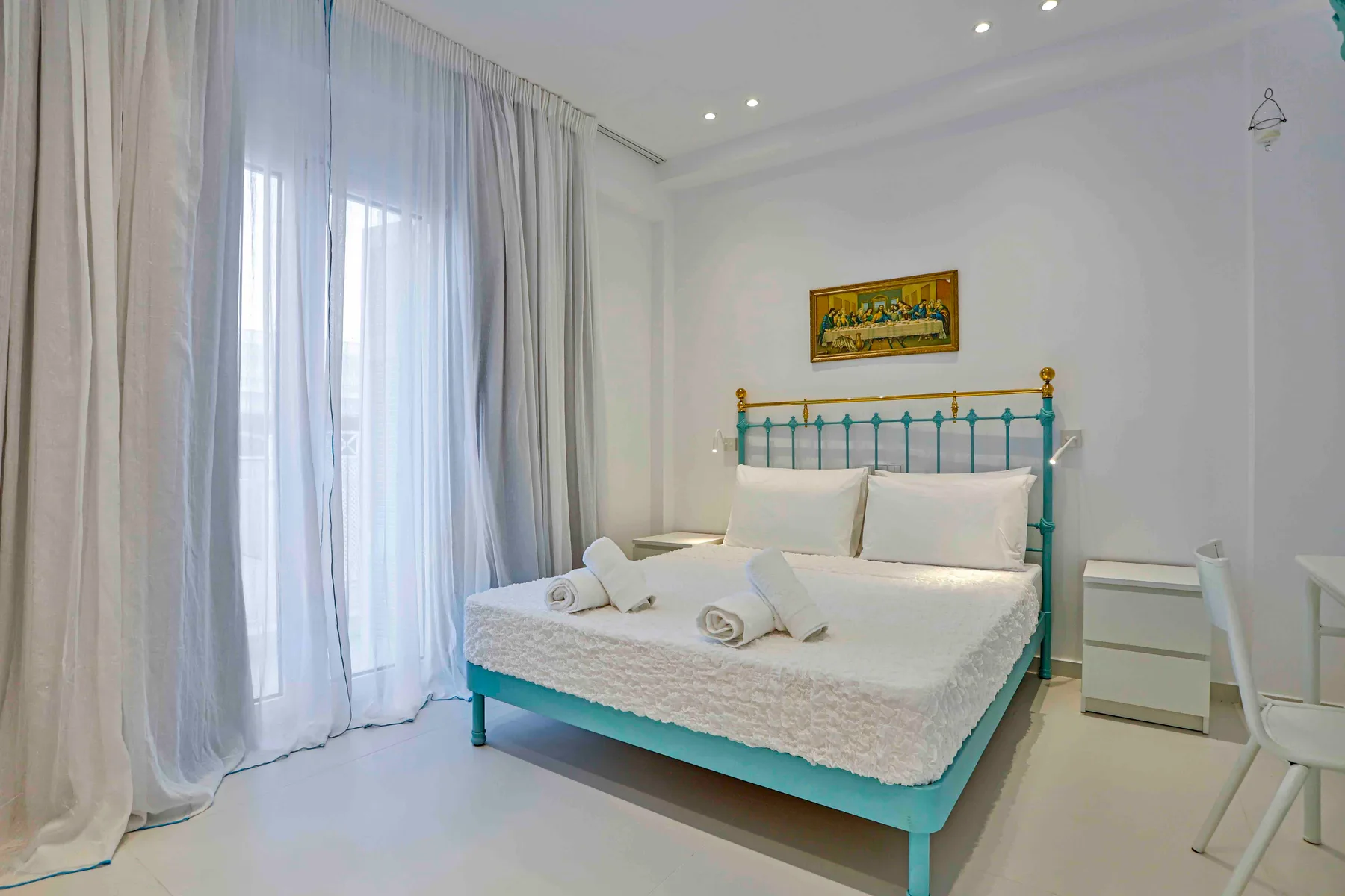 Un dormitorio con una cama verde azulado y ventanas altas con cortinas.