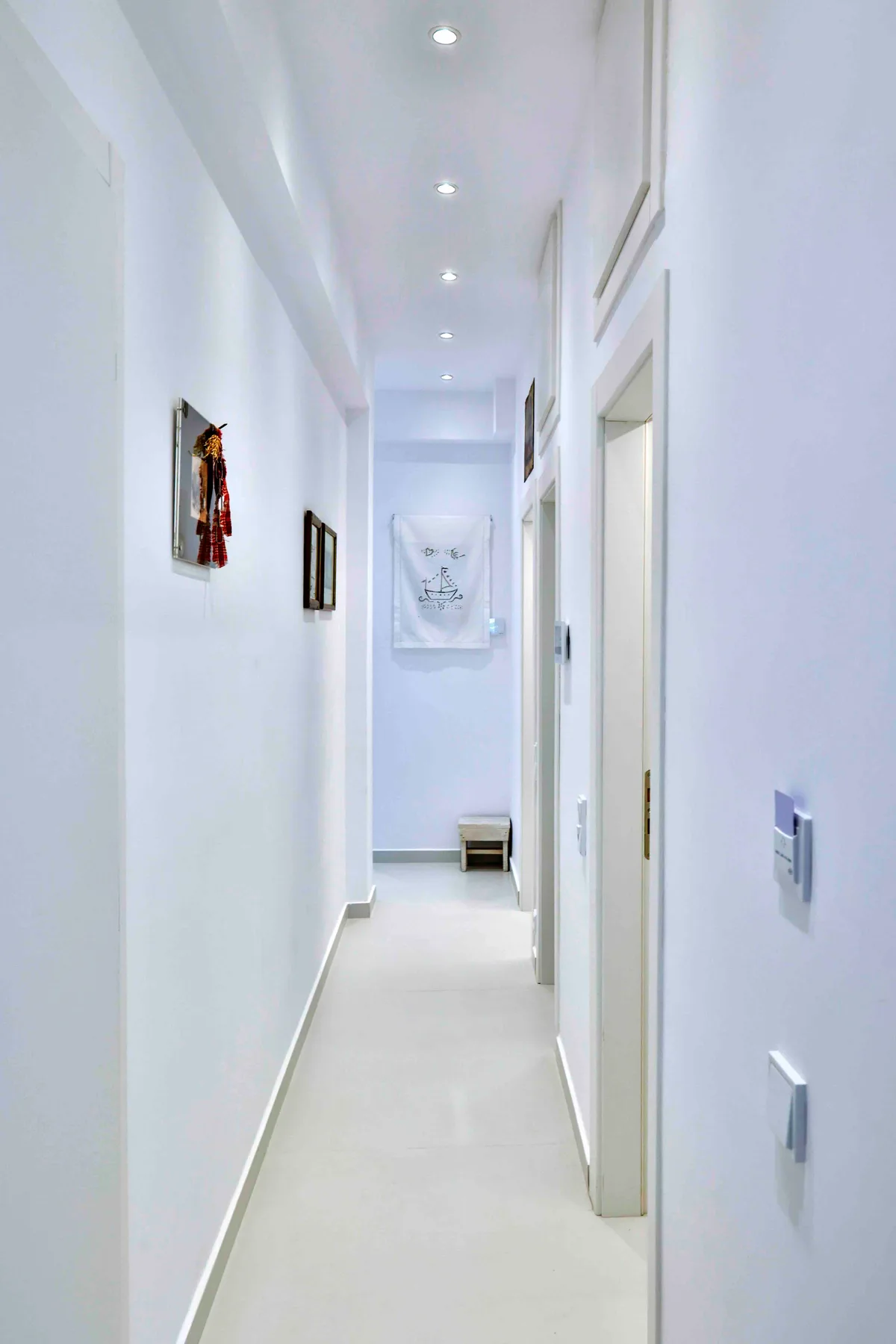A bright, narrow hallway with white walls and framed artwork.