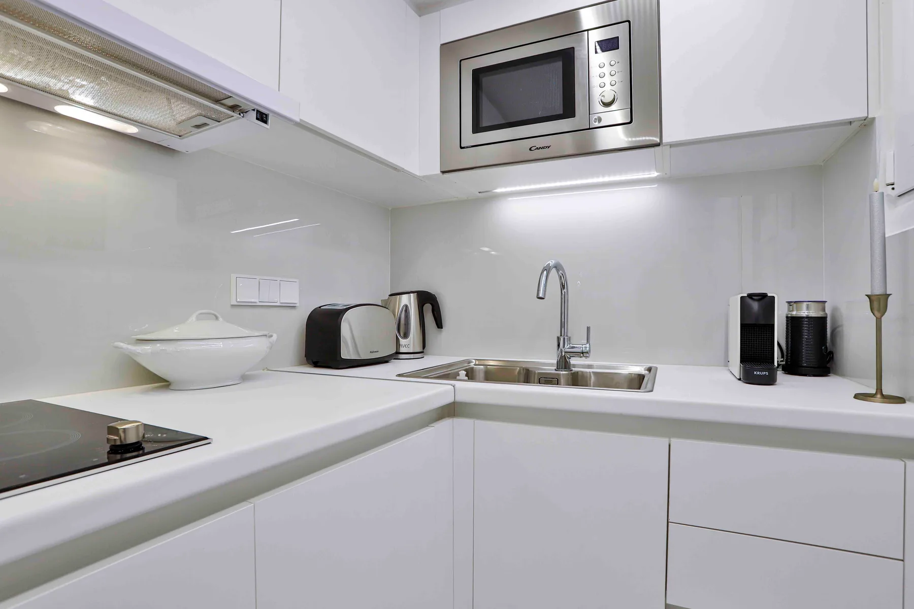 A bright white kitchen with a cooktop, sink, and built-in microwave.