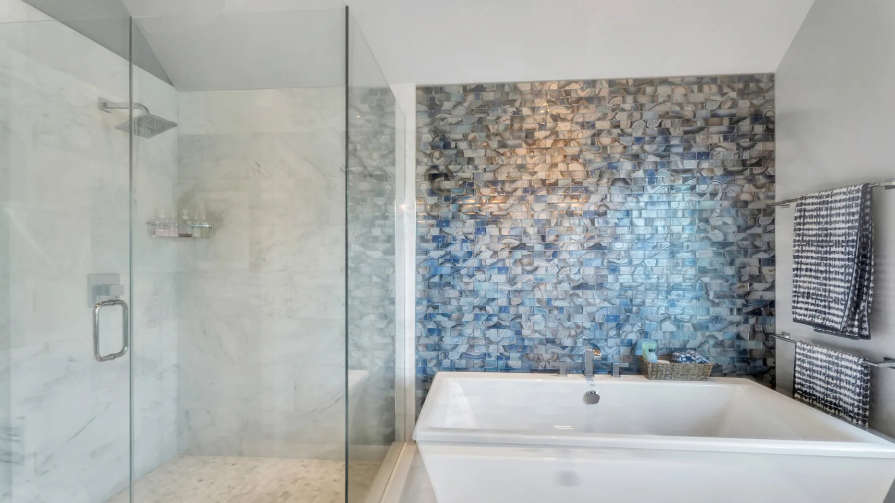Un baño con bañera, ducha de vidrio y una pared estampada.