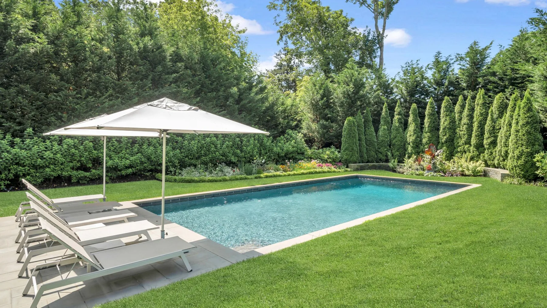 An outdoor swimming pool with lounge chairs beneath a large white umbrella.