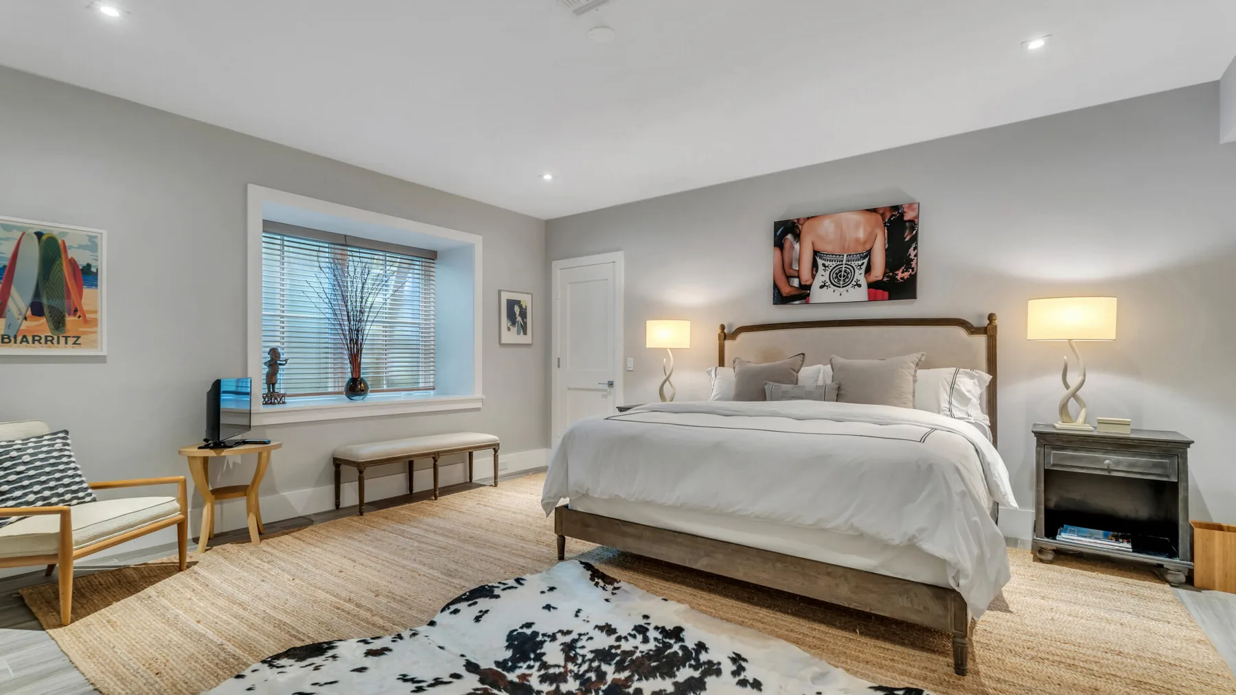 Un dormitorio luminoso con una cama grande, mesitas de noche y una ventana con persianas.