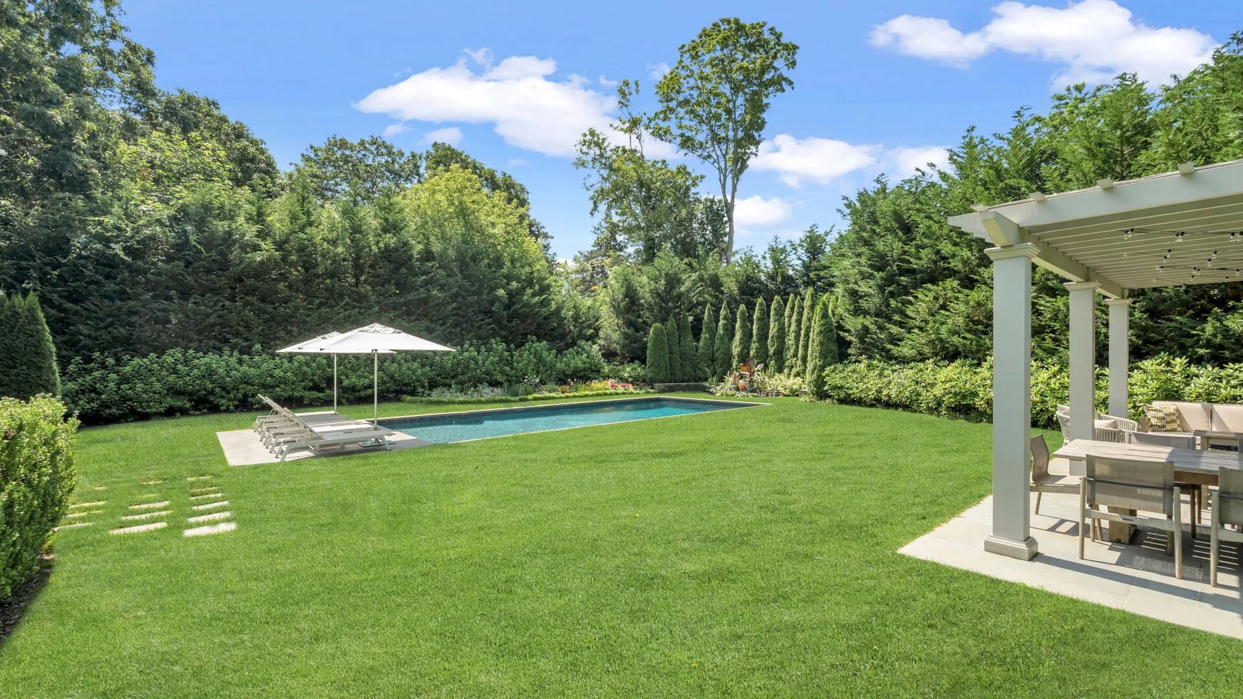 A landscaped backyard with a swimming pool, lawn, and covered dining area.