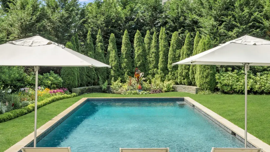 Una piscina al aire libre está rodeada de vegetación y tiene sombrillas para dar sombra.