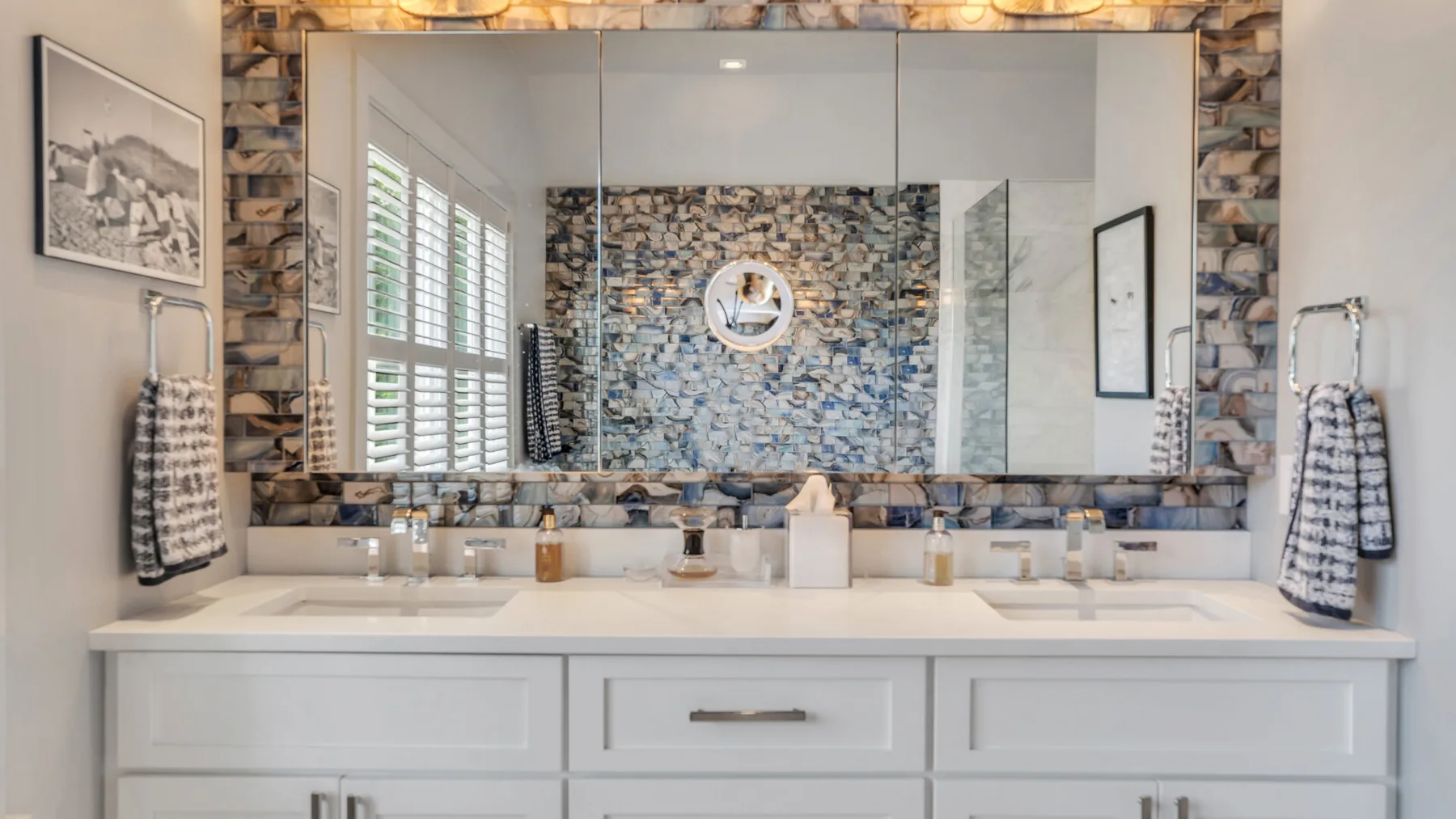 Un tocador de baño con un espejo amplio y un salpicadero de azulejos estampados.