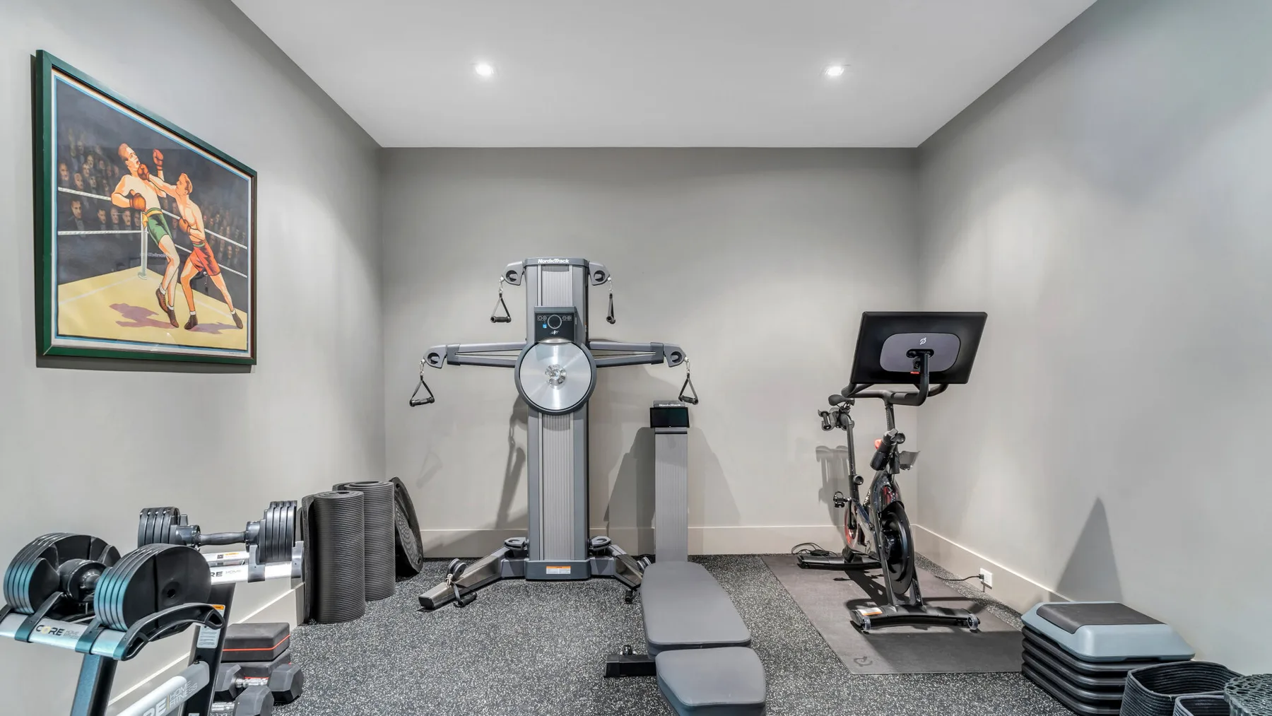 Un gimnasio en casa con equipo de ejercicio y un cuadro deportivo en la pared.
