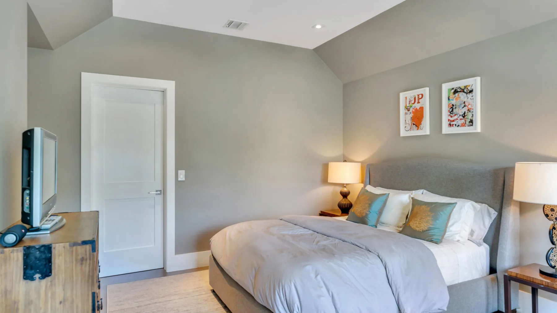 Un dormitorio con una cama, mesitas de noche y cuadros en la pared.
