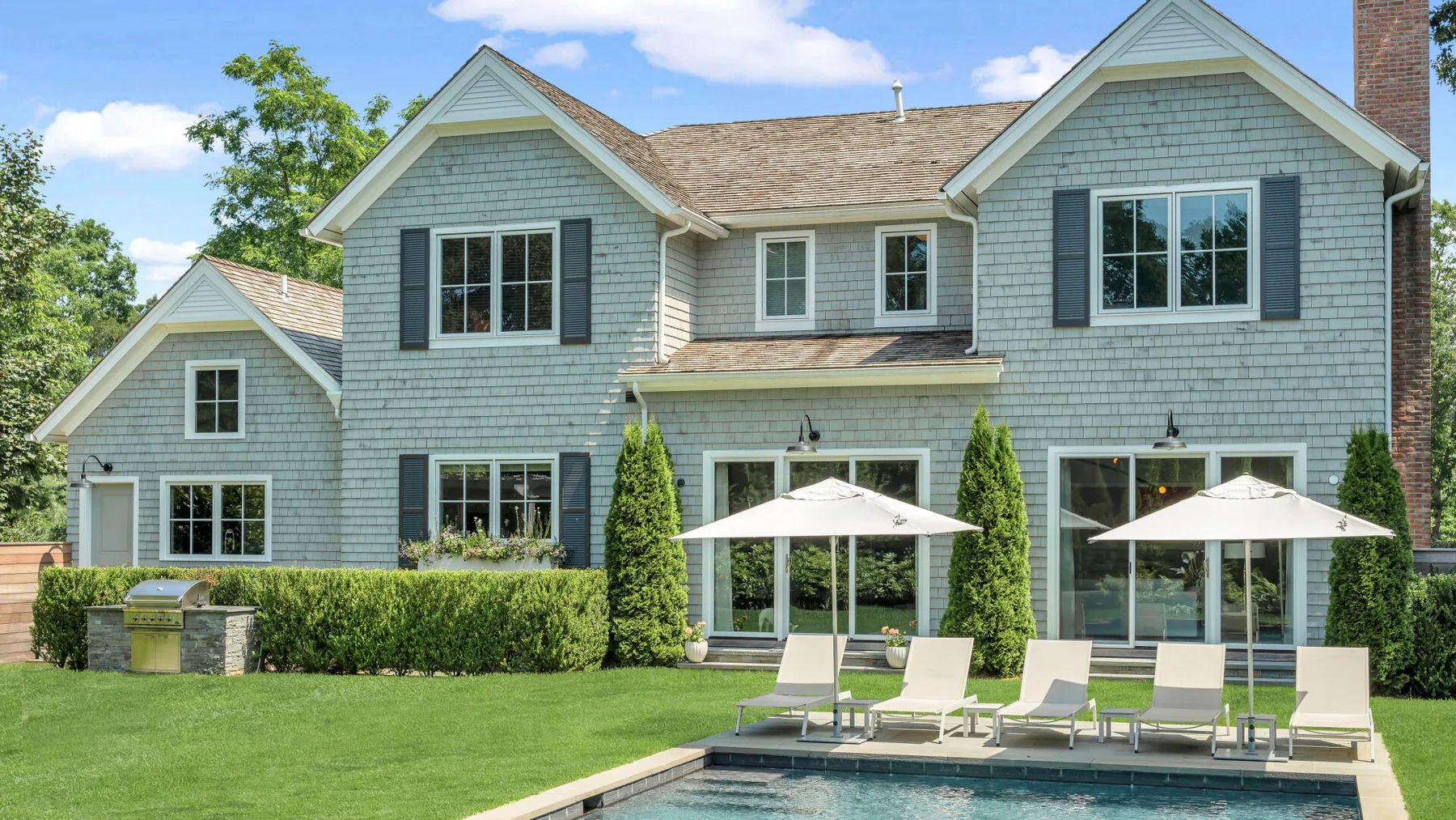 Una casa grande con césped, piscina y sombrillas de patio.