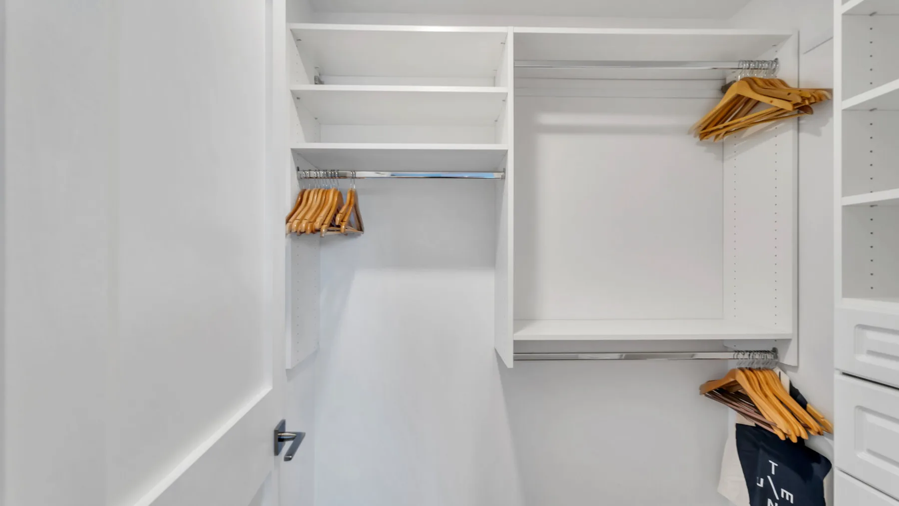 Un armario vestidor blanco tiene estantes abiertos y barras para colgar con perchas de madera.