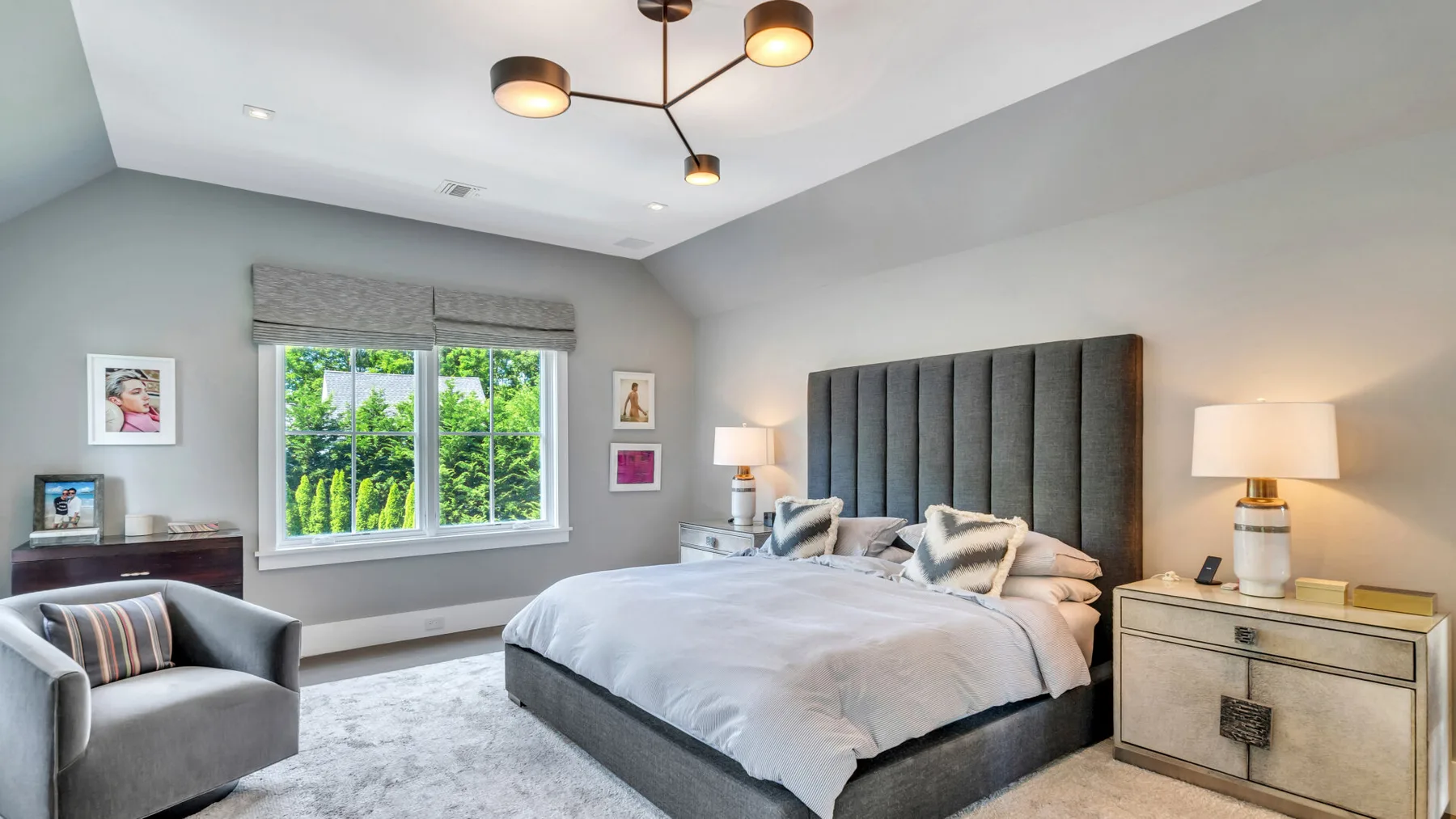 Un dormitorio con una cama grande, mesitas de noche y un sillón gris.