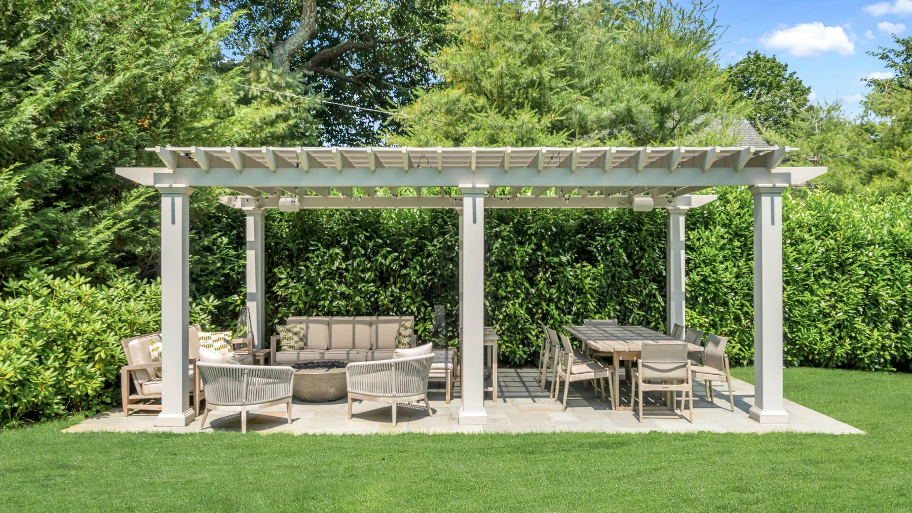 Un patio ajardinado con una pérgola blanca, asientos al aire libre y una mesa de comedor.