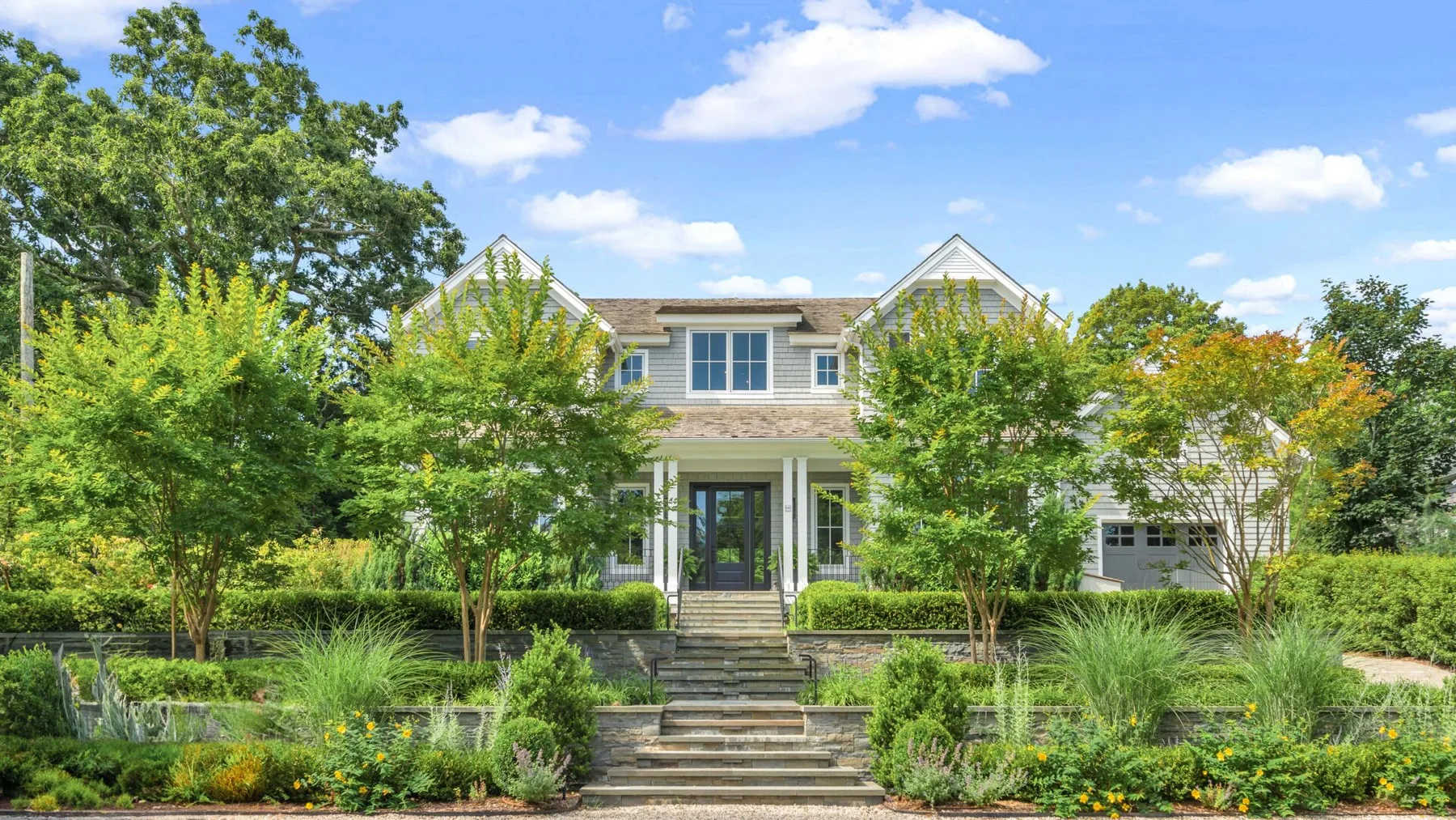 A large house stands behind landscaped gardens and a broad stone staircase.