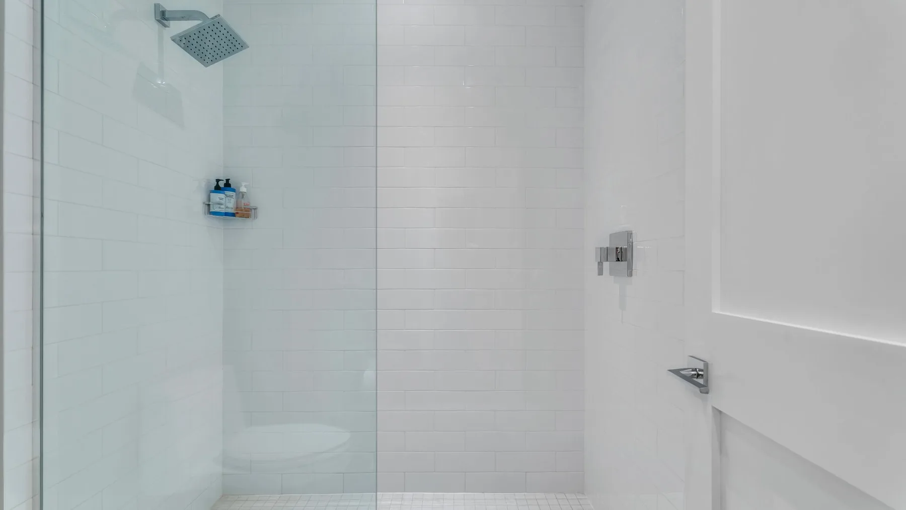 Una zona de ducha con azulejos, una mampara de vidrio y un cabezal de ducha en la pared.