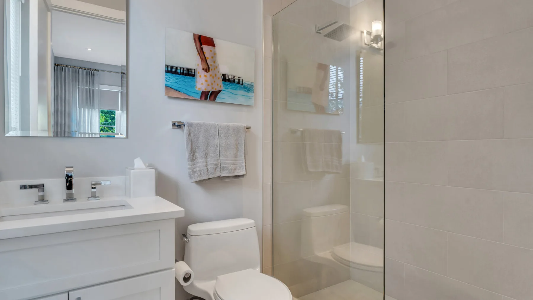 Un baño luminoso con lavabo blanco, inodoro y ducha de cristal.