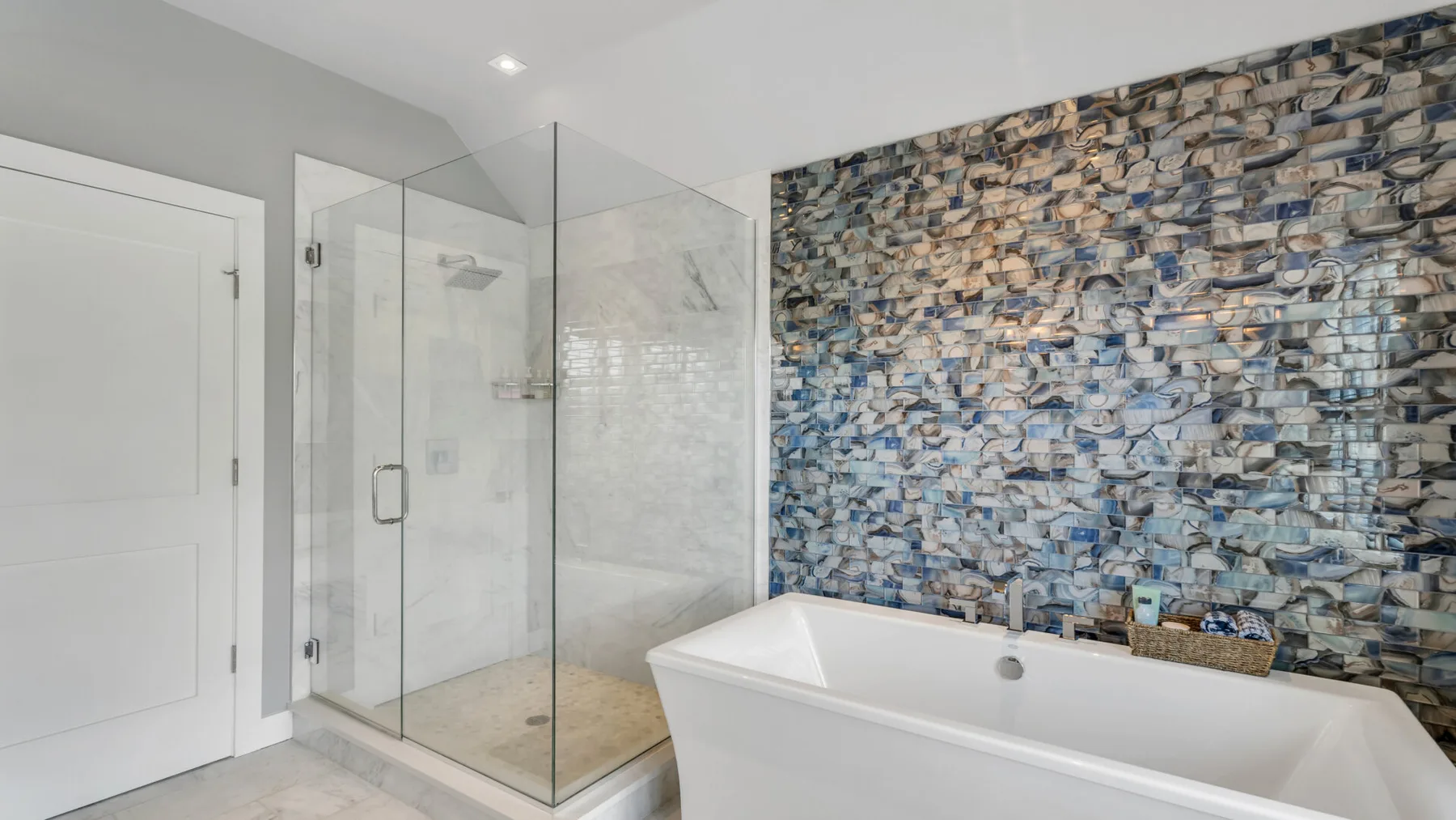 Un baño con bañera, ducha de vidrio y pared de azulejos estampados.