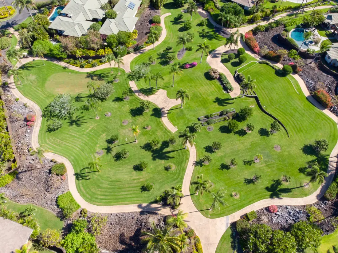 An aerial view shows landscaped green grounds with winding paths and scattered palms.