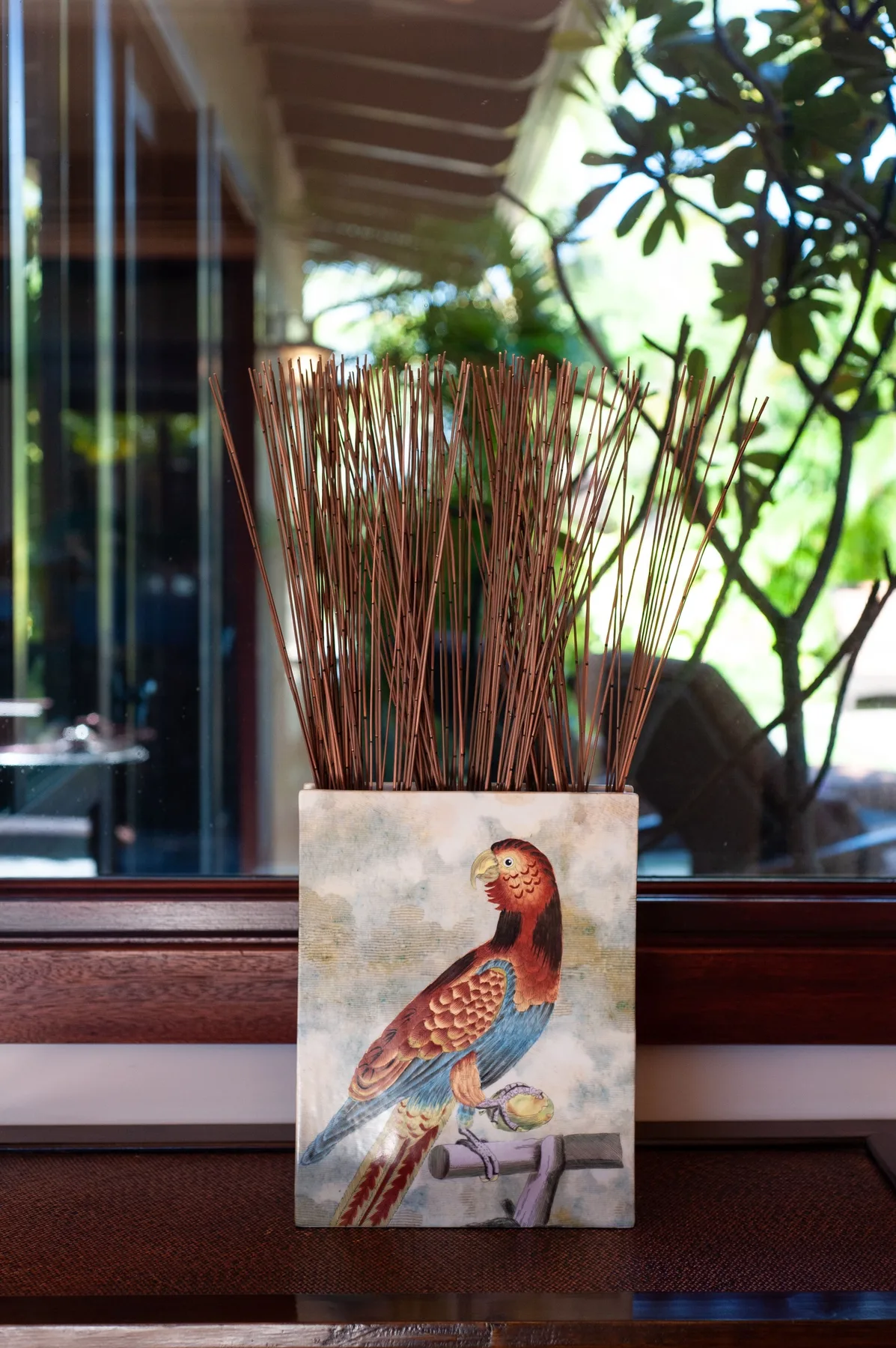 A decorative bird illustration sits beneath tall dried stems on a window ledge.